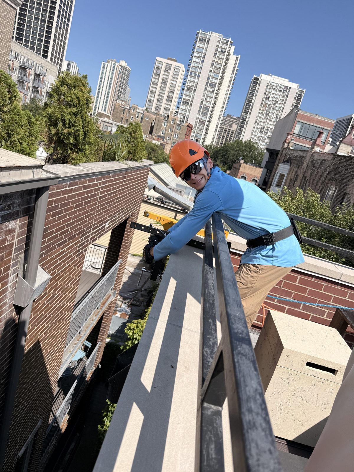 Kobicos rope access technician on the roof of a four-story Old Town building, Chicago high-rises behind